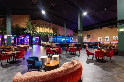 Salle de restaurant moderne avec bar illuminé, tables en bois, chaises colorées et décoration murale végétale.