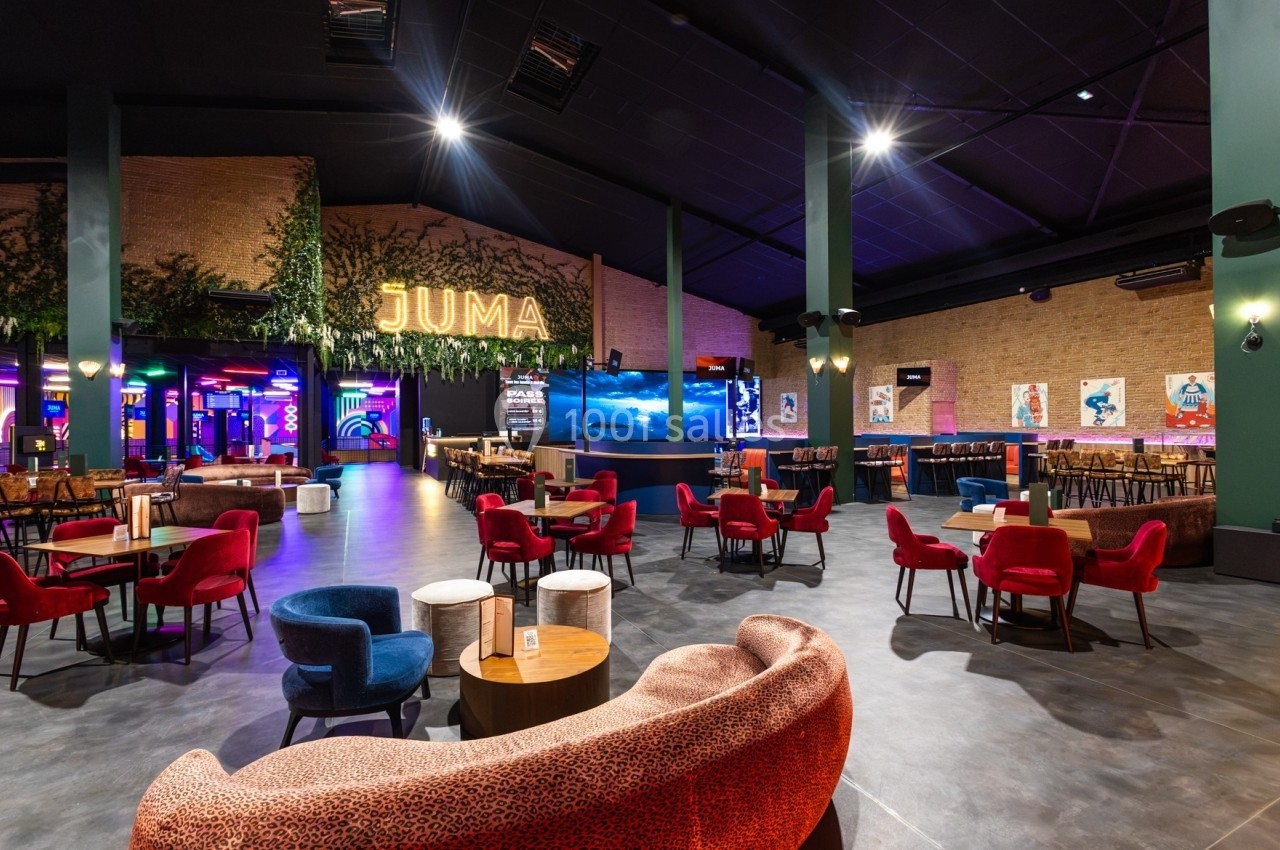 Salle spacieuse avec tables et fauteuils colorés, éclairage chaleureux, décorations murales et enseigne lumineuse ’JUMA’.