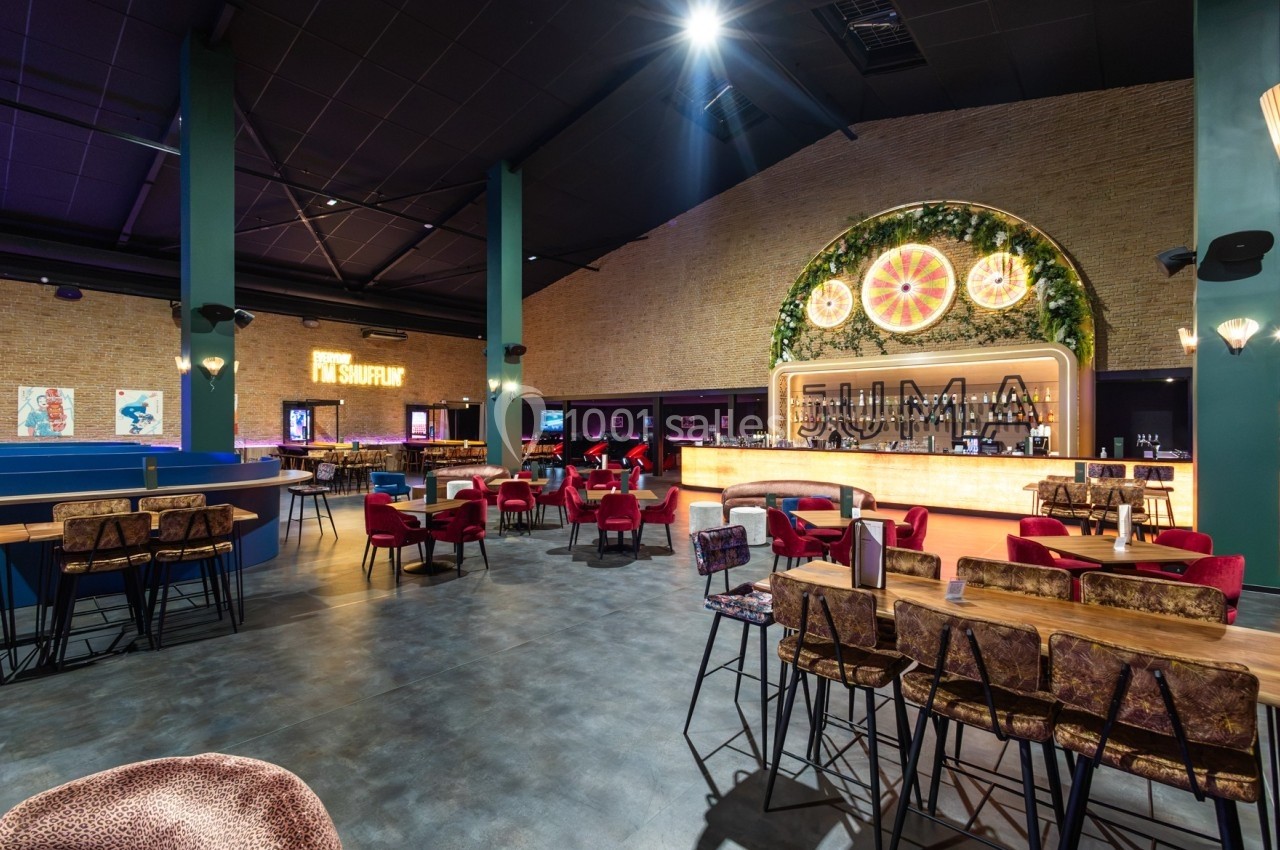 Salle de restaurant moderne avec bar illuminé, tables en bois, chaises colorées et décoration murale végétale.