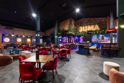 Salle de restaurant moderne avec bar illuminé, tables en bois, chaises colorées et décoration murale végétale.