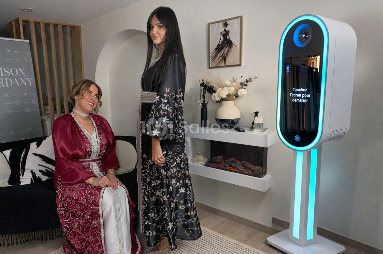 Deux femmes en robes traditionnelles posent près d'une borne photo interactive dans un intérieur élégant.
