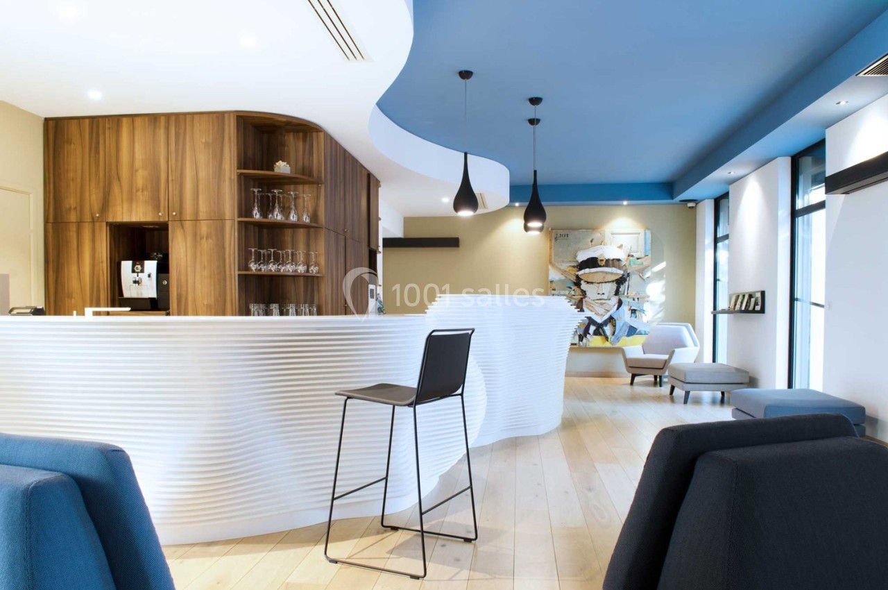 Intérieur moderne avec comptoir blanc ondulé, chaises design, éclairage suspendu et décor mural artistique.