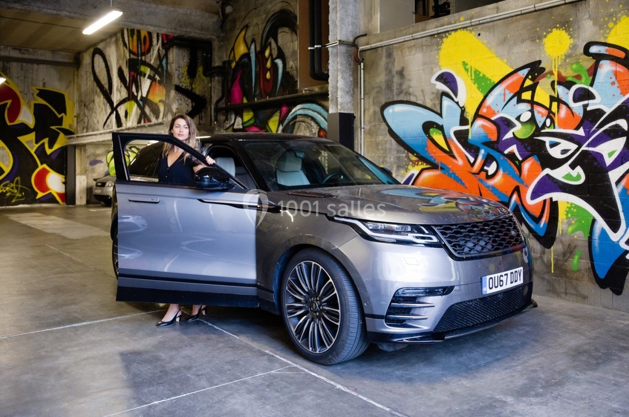 Une femme sort d'un SUV gris stationné dans un garage aux murs décorés de graffitis colorés.