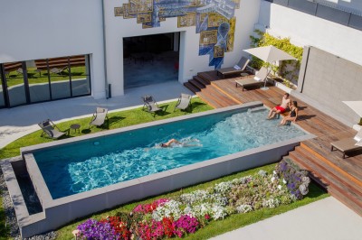 Chambre lumineuse avec lit double, table en bois, chaise beige, miroir et grande fenêtre avec stores.