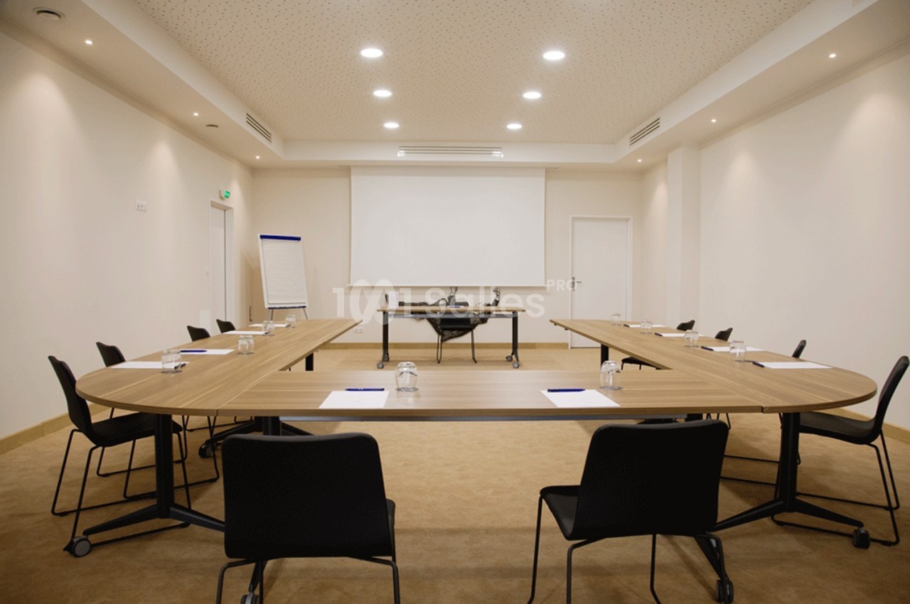 Salle de réunion moderne avec tables en U, chaises noires, tableau de conférence et projecteur.