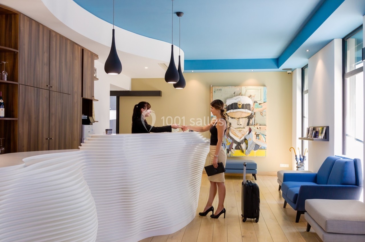 Une femme en talons échange avec une réceptionniste derrière un comptoir moderne dans un hall lumineux.