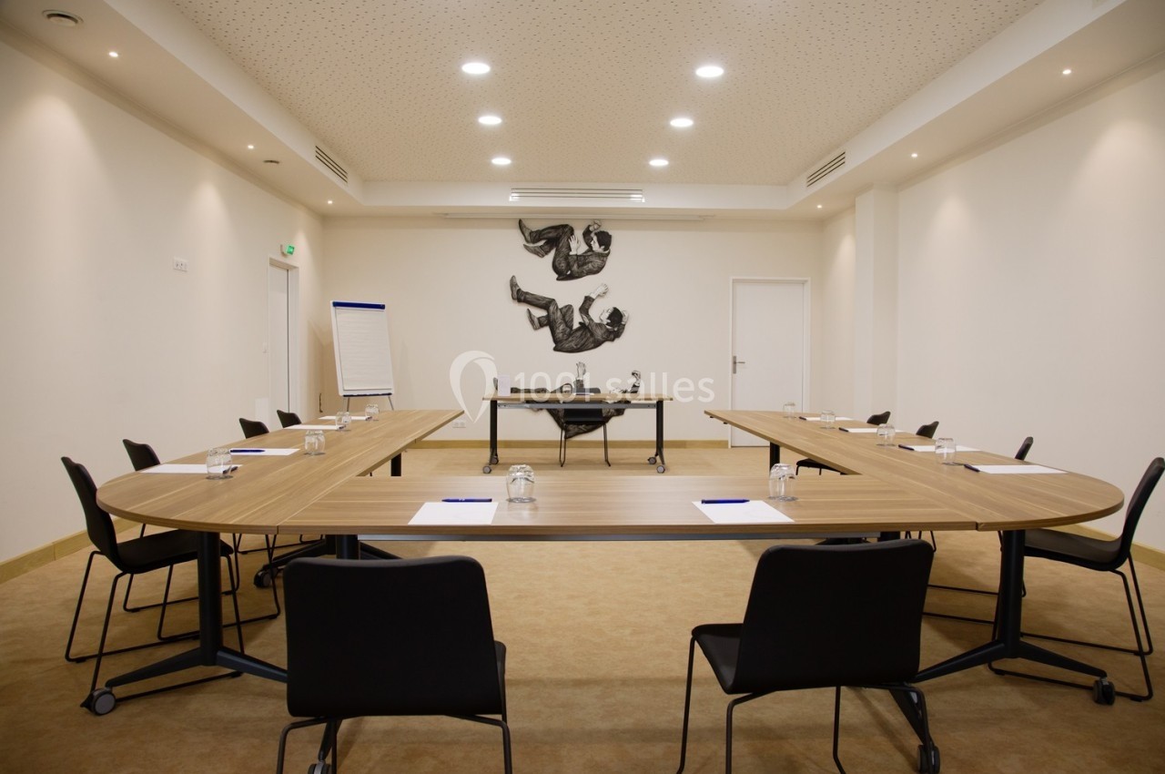 Salle de réunion lumineuse avec tables en U, chaises noires, tableau de conférence et décoration murale artistique.
