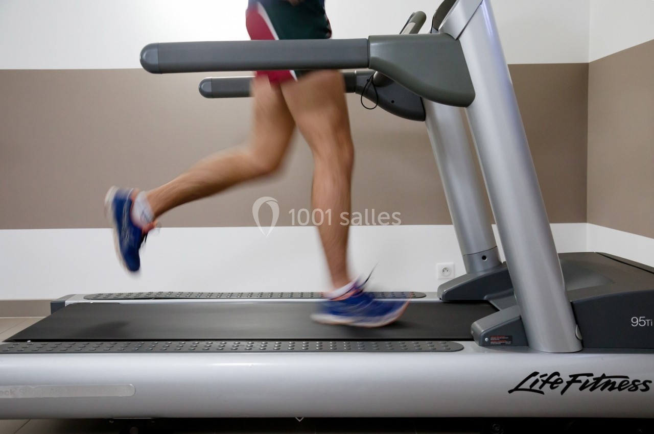 Un homme court sur un tapis de course dans une pièce aux murs beige et blanc.
