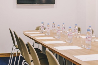 Chambre lumineuse avec lit double, table en bois, chaise beige, miroir et grande fenêtre avec stores.