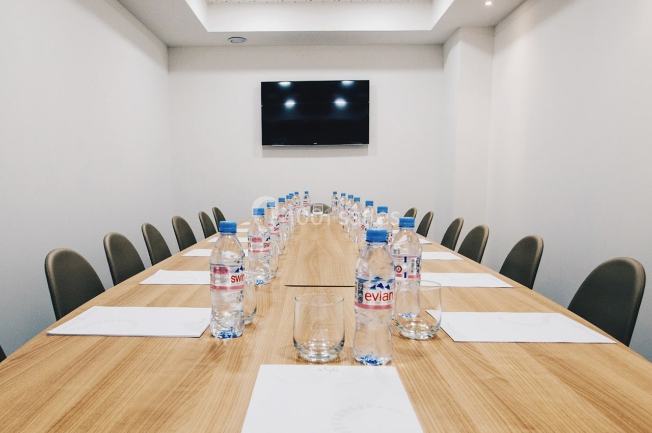 Salle de réunion avec une longue table en bois, des chaises, des bouteilles d'eau et un écran mural.