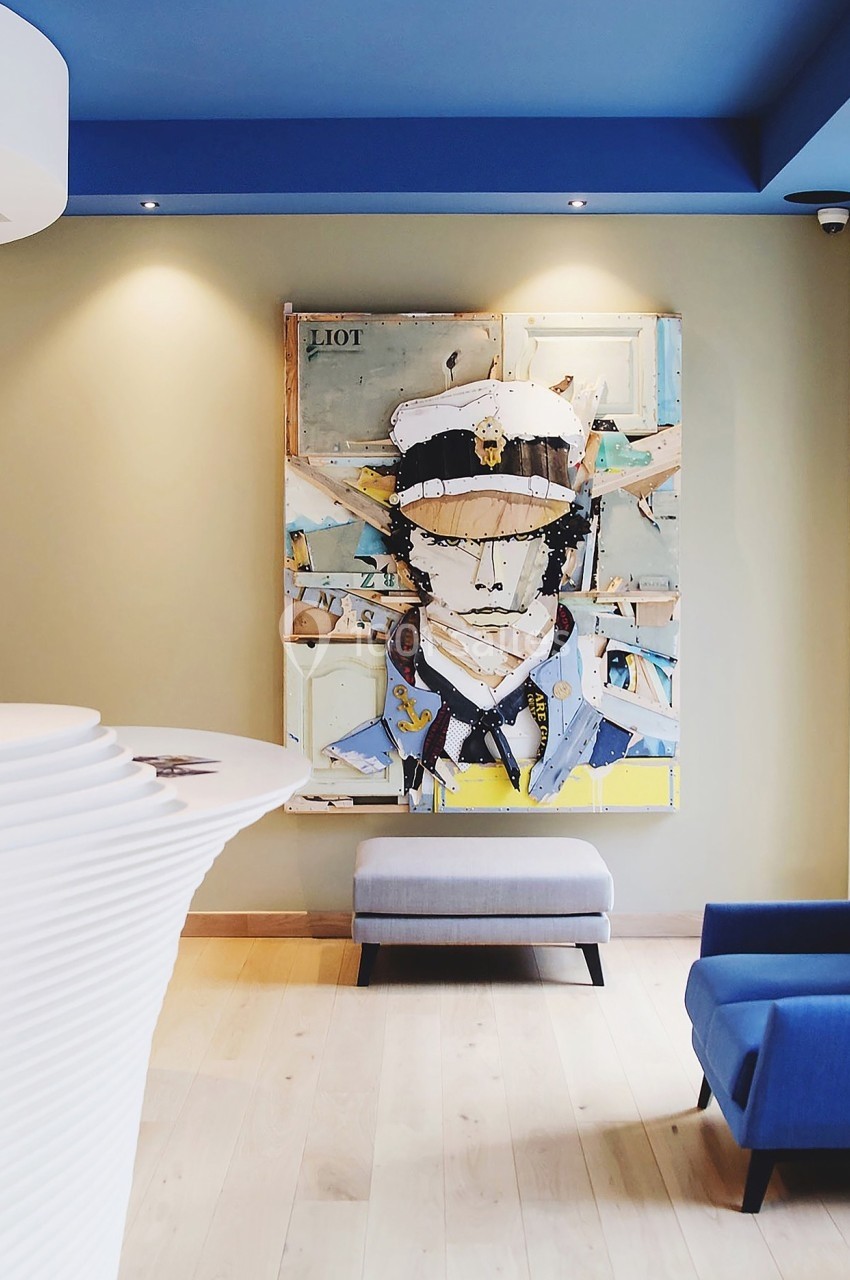 Tableau coloré représentant un personnage en uniforme, accroché sur un mur beige dans un espace moderne avec fauteuils bleus.