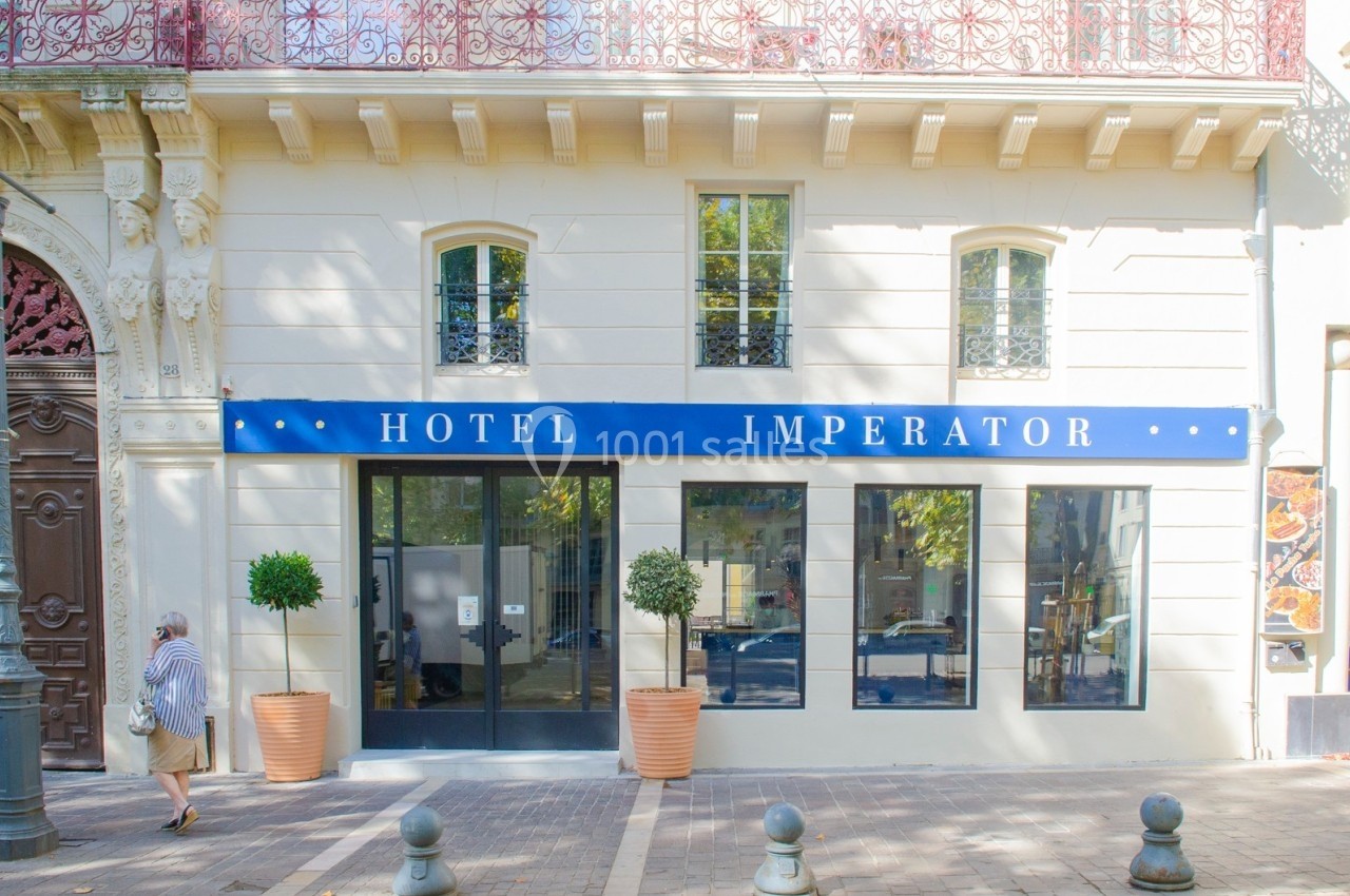Façade d'un hôtel avec une enseigne bleue ’Hotel Imperator’, grandes fenêtres et deux arbres en pot devant l'entrée.