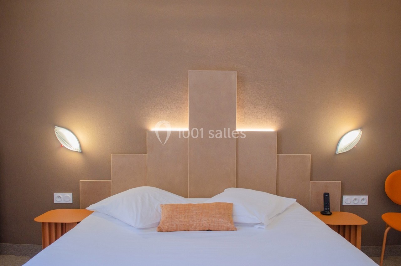 Lit double avec tête de lit géométrique éclairée, deux tables de chevet en bois et deux appliques murales.