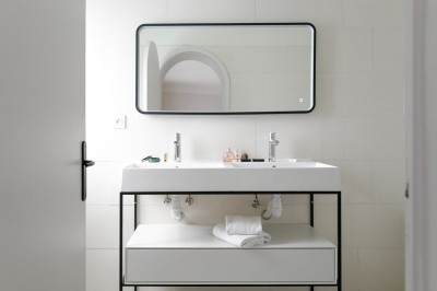 Salle de bain lumineuse avec un double lavabo, un grand miroir, une baignoire et des murs carrelés clairs.
