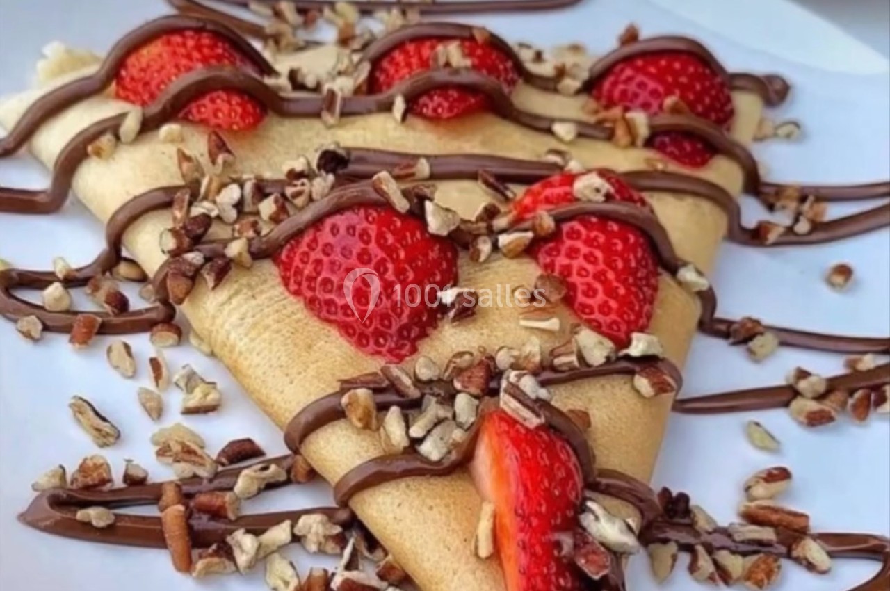 Crêpe garnie de fraises fraîches, nappée de chocolat et parsemée de morceaux de noix sur une assiette blanche.