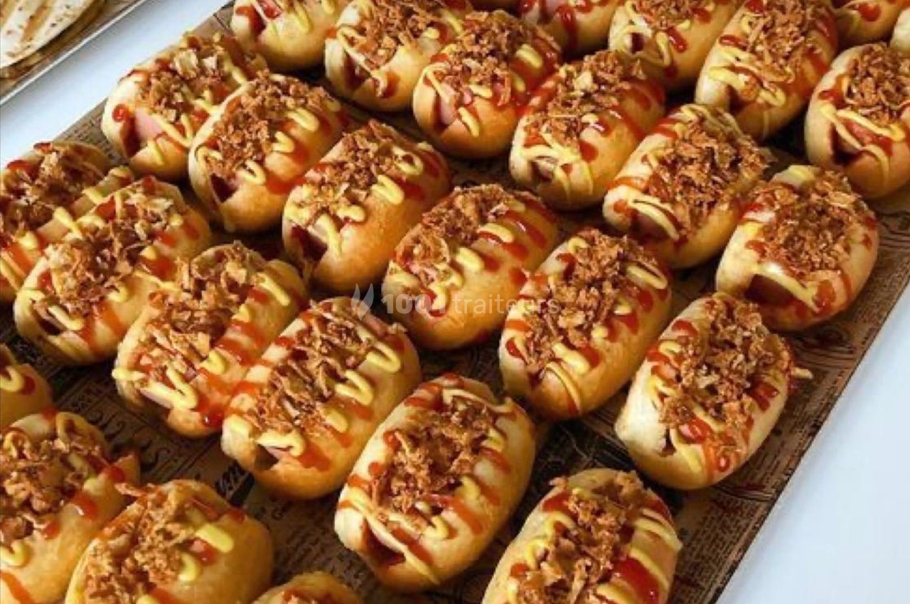 Plateau de petits pains garnis de sauce, moutarde et oignons frits, disposés en rangées serrées.