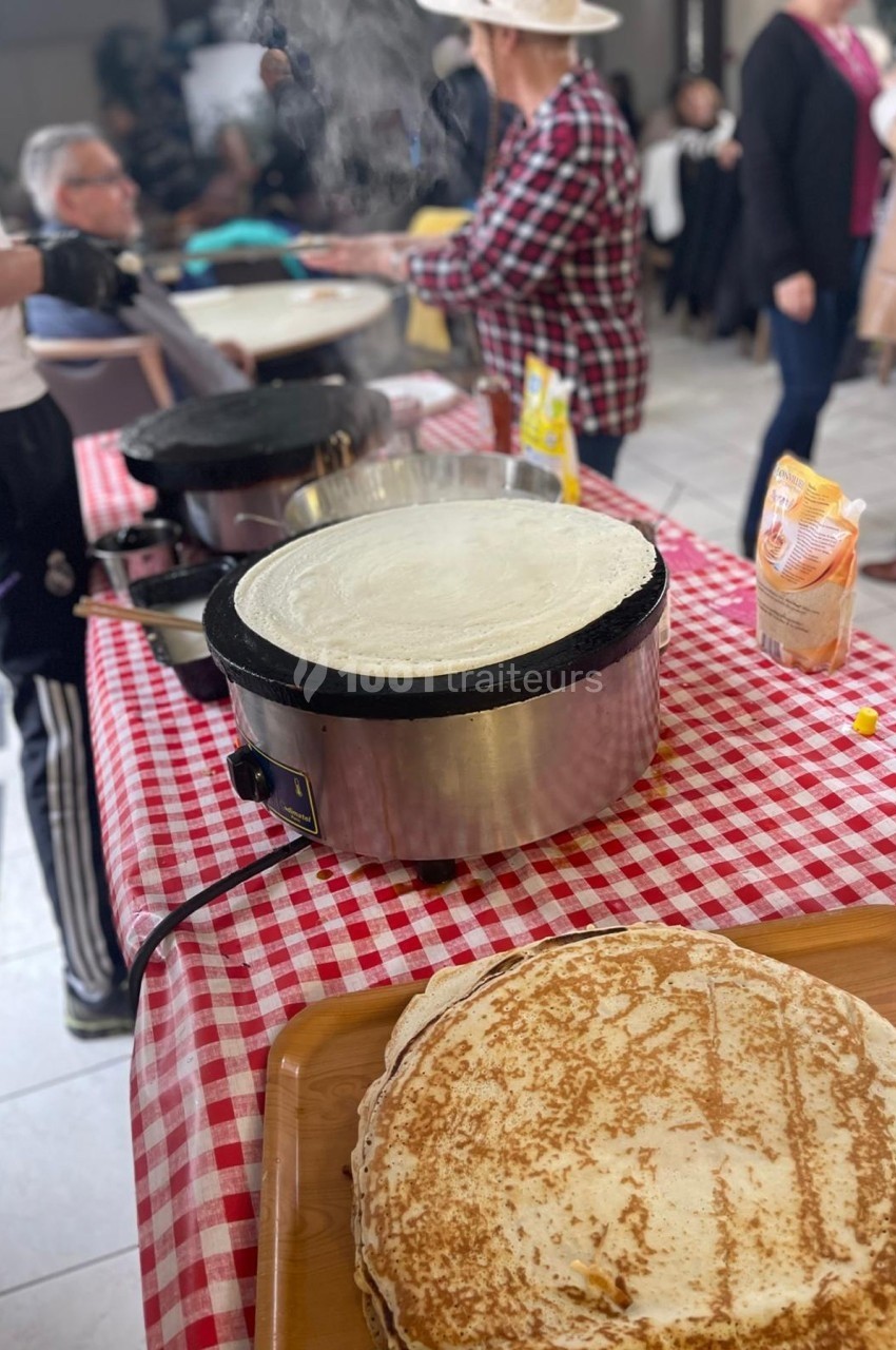 Des crêpes en cours de préparation sur des crêpières électriques, avec des personnes en arrière-plan.