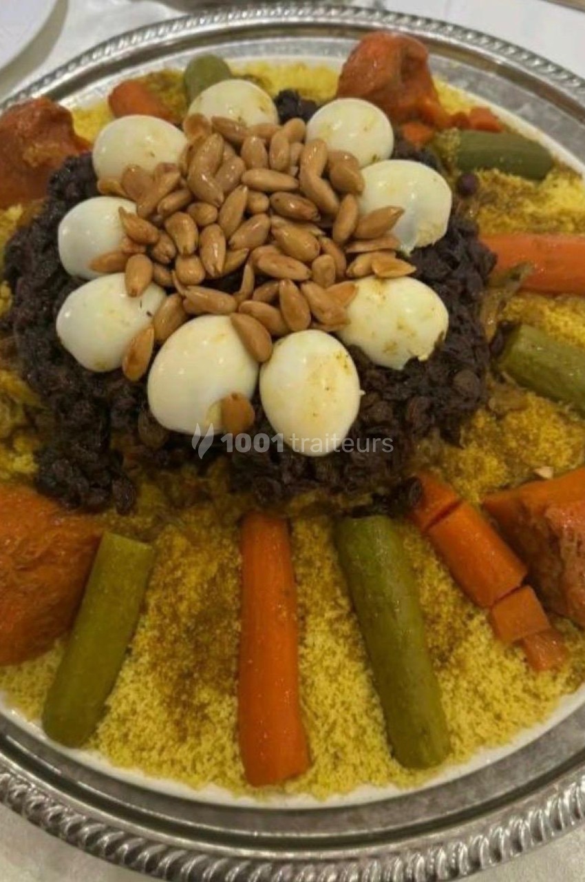 Plat de couscous garni de légumes, viande, œufs durs, raisins secs et amandes, présenté sur un grand plateau.