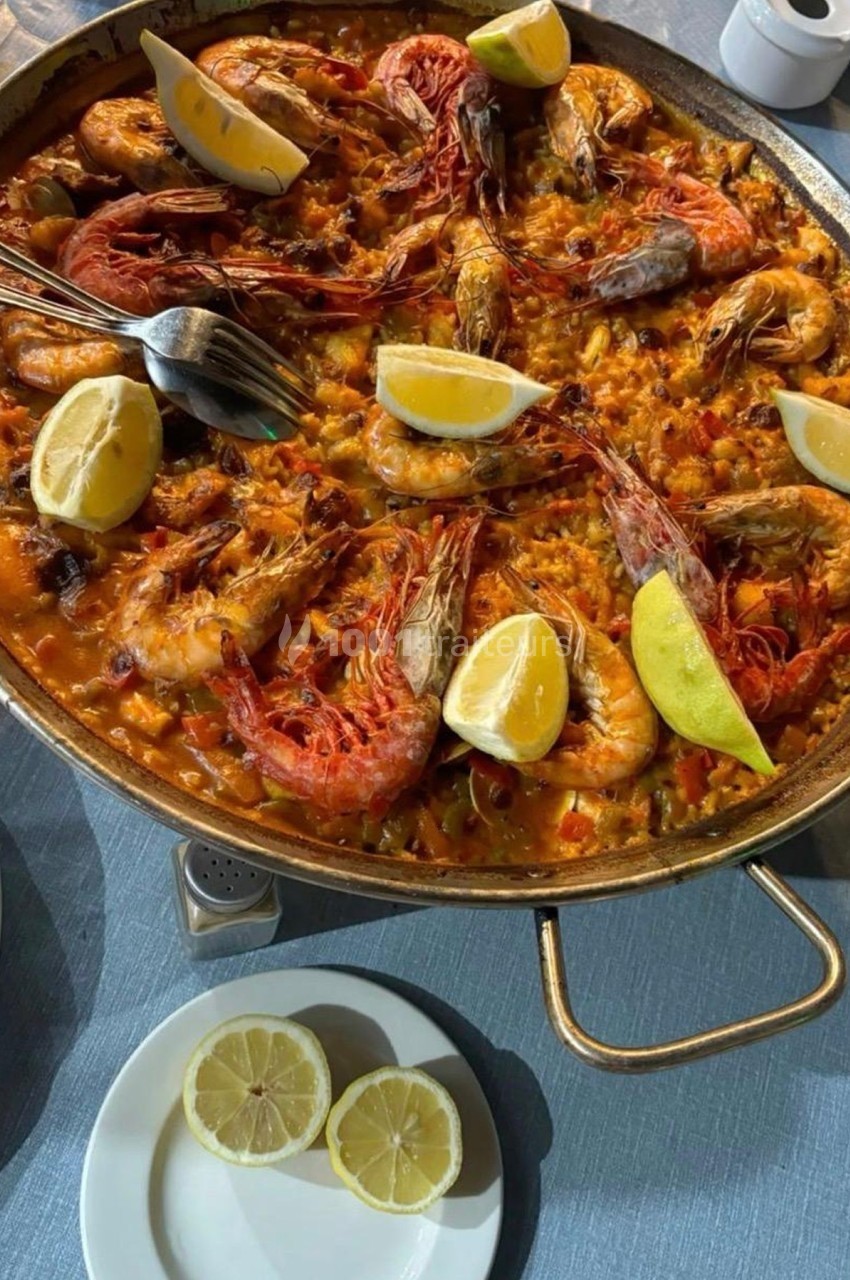 Plat de paella aux fruits de mer avec crevettes, citron et riz safrané, servi dans une grande poêle sur une table.