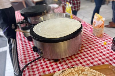 Des crêpes en cours de préparation sur des crêpières électriques, avec des personnes en arrière-plan.
