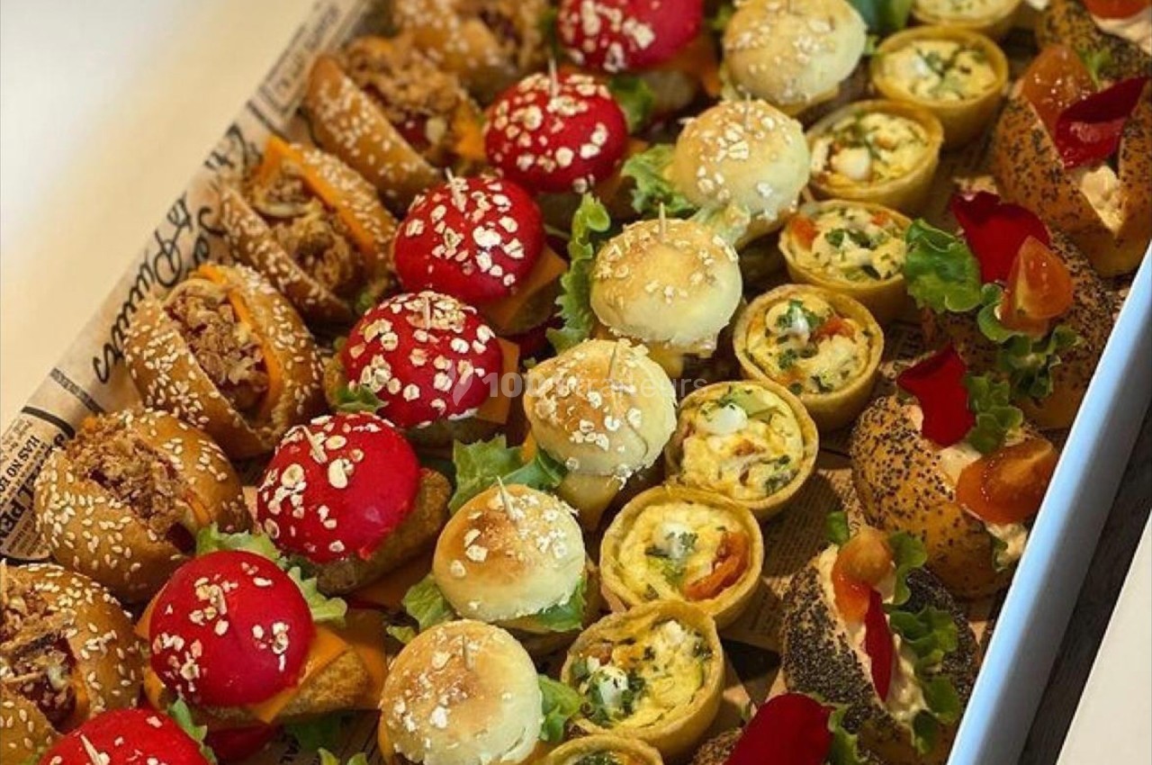 Plateau de bouchées variées comprenant mini-sandwichs, feuilletés et roulés garnis de légumes et graines.