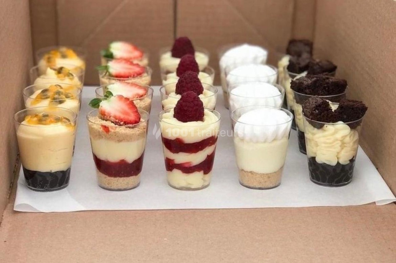 Assortiment de verrines sucrées variées avec fruits, mousse et chocolat, disposées dans une boîte en carton.