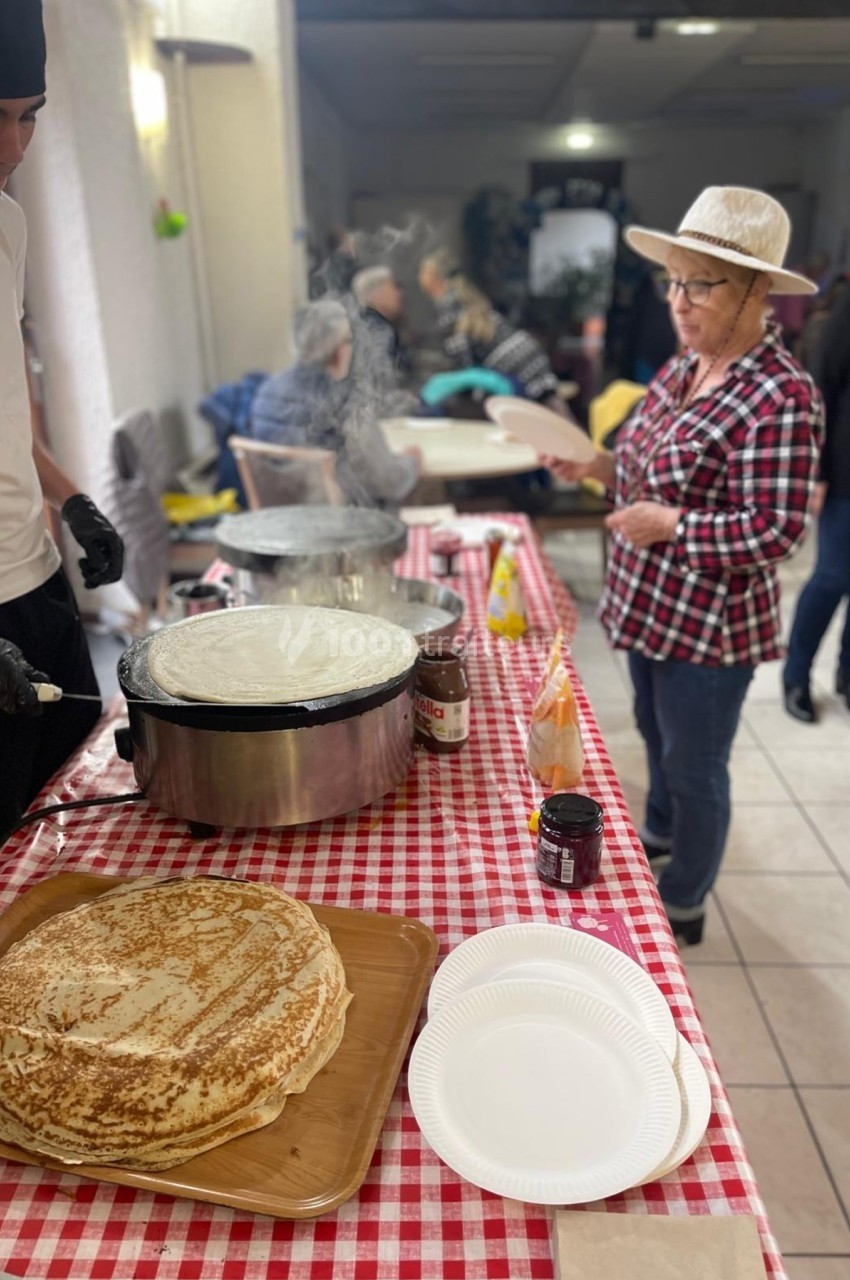 Un stand de crêpes avec un cuisinier en action et une femme attendant, dans une salle animée.
