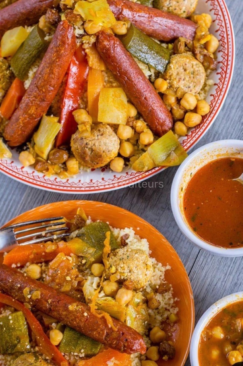 Assiette de couscous garni de légumes, merguez, boulettes et pois chiches, accompagnée de sauce rouge.