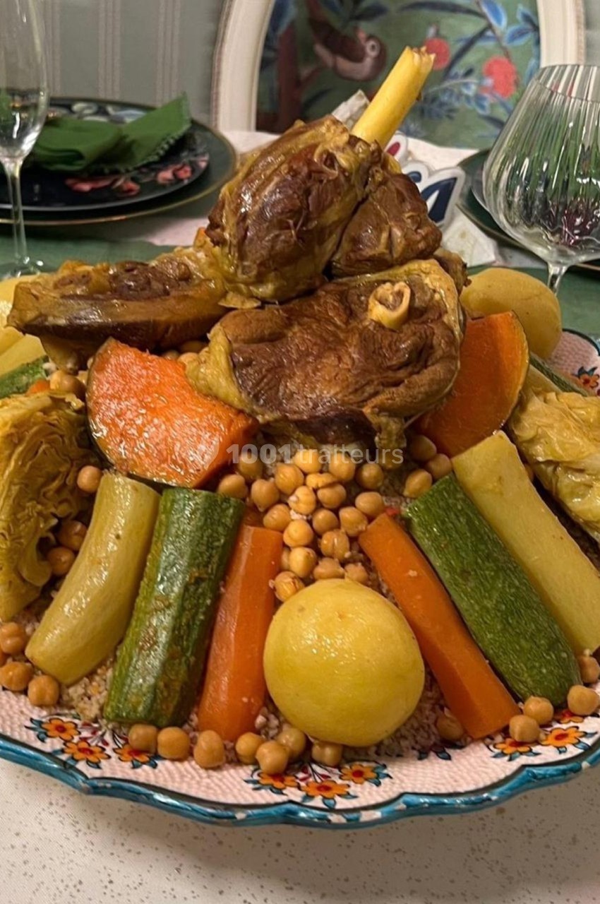 Plat de couscous garni de légumes variés, pois chiches et morceaux de viande, présenté dans un grand plat décoré.