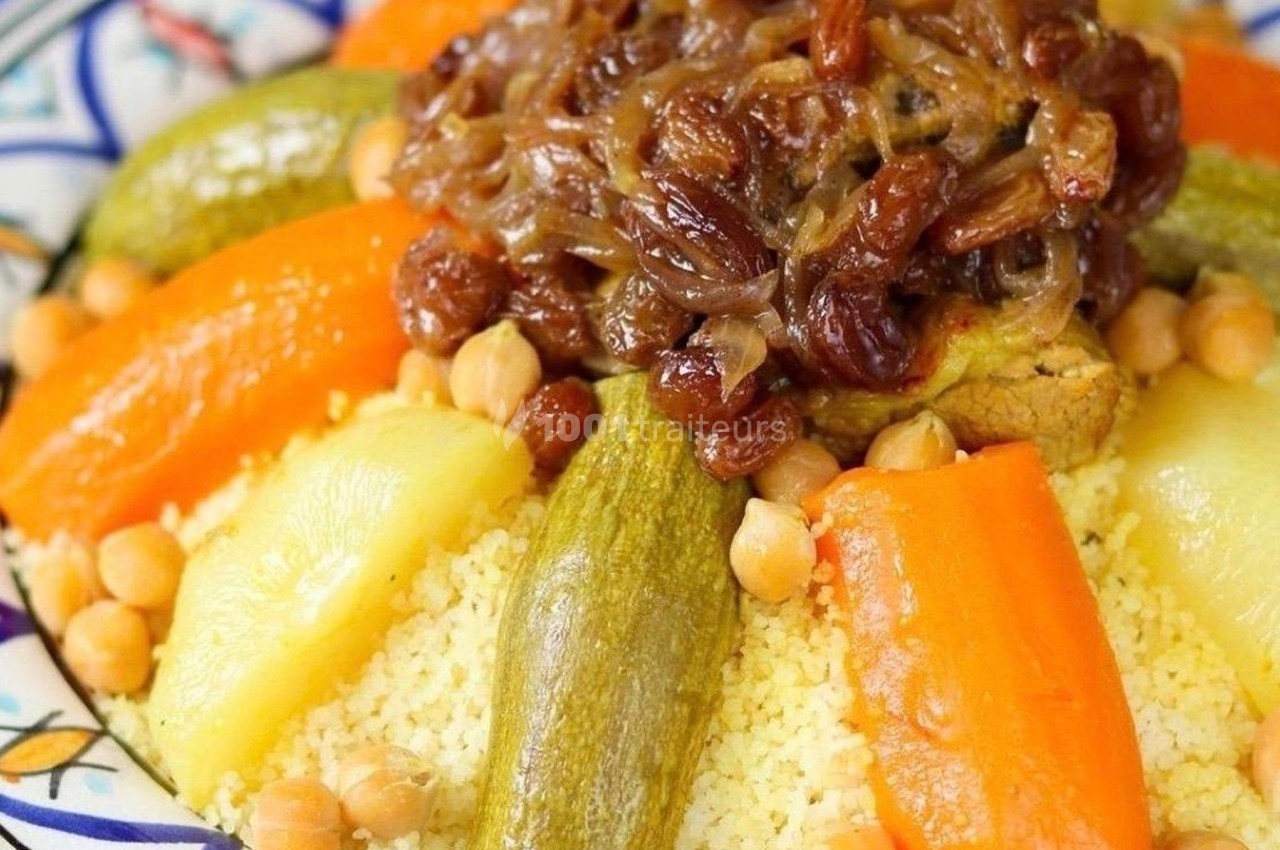 Plat de couscous garni de légumes variés, pois chiches, raisins secs et oignons caramélisés, présenté dans une assiette…