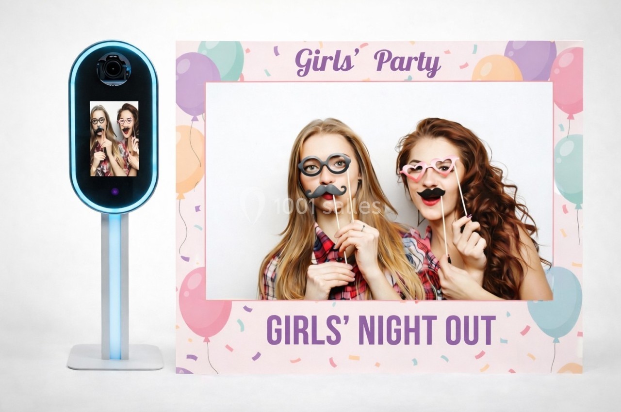 Deux femmes posent avec des accessoires amusants devant un cadre décoré pour une soirée entre filles.