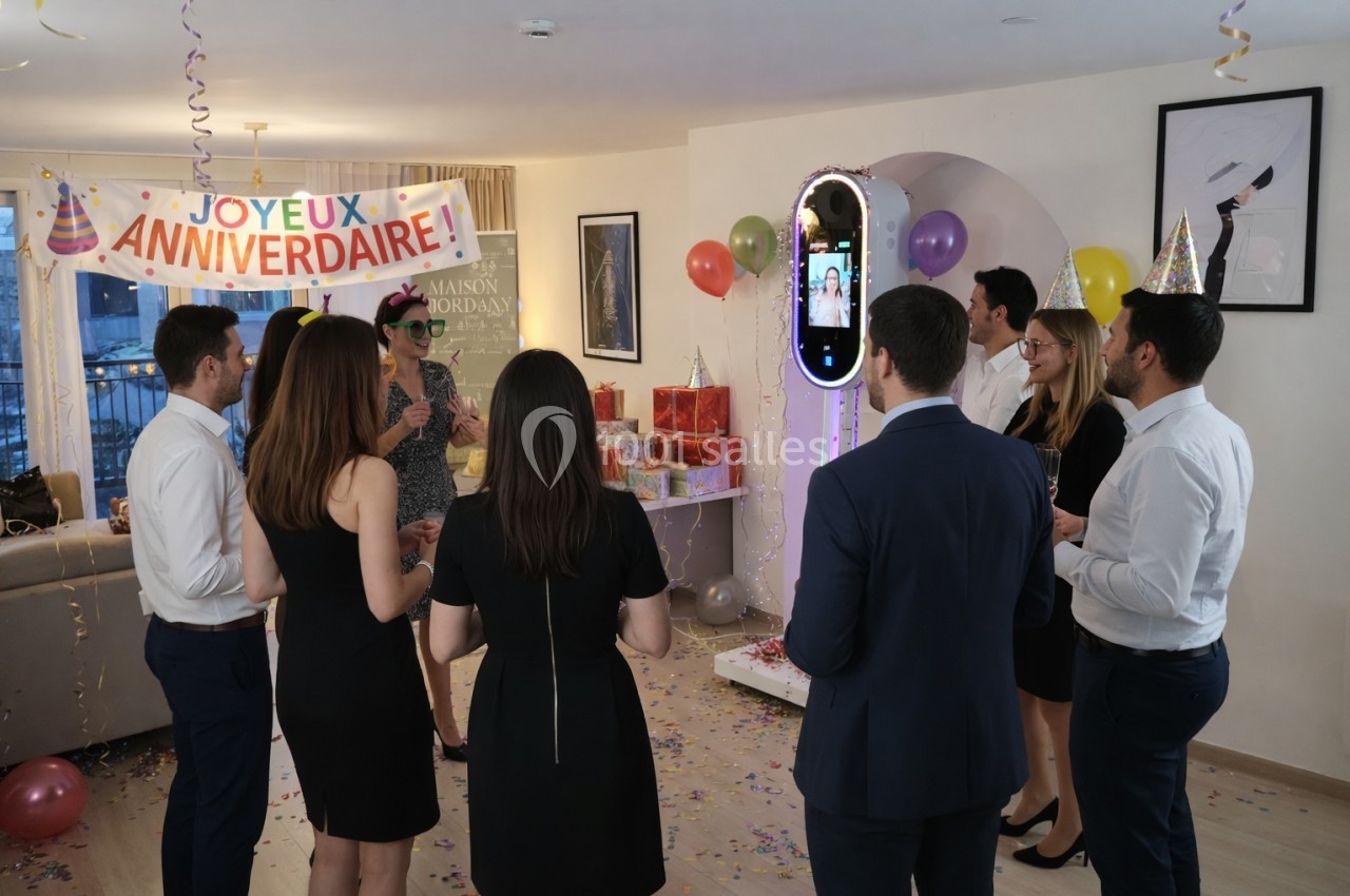 Un groupe de personnes fête un anniversaire dans un salon décoré avec des ballons et une banderole.