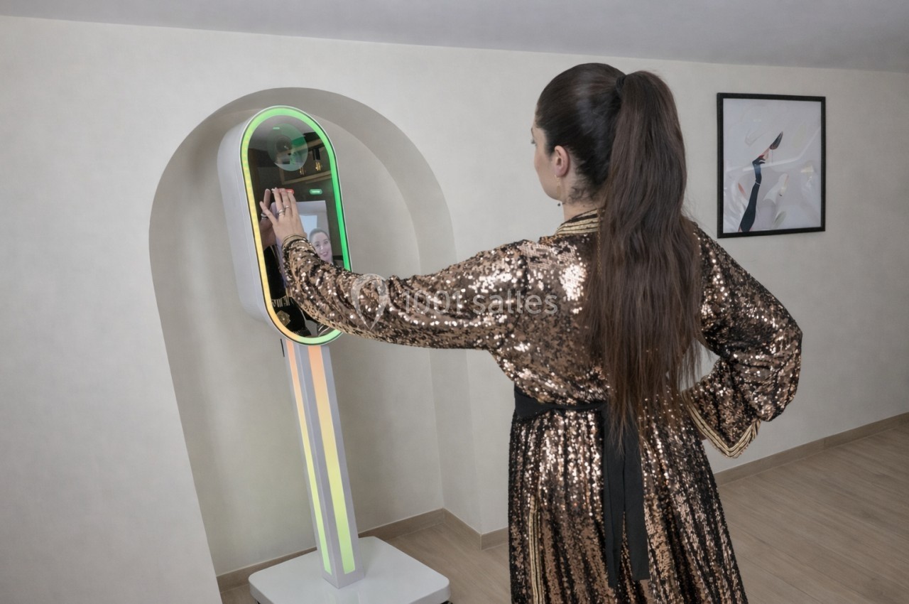 Une femme en robe à paillettes interagit avec une borne photo lumineuse dans une pièce au décor minimaliste.