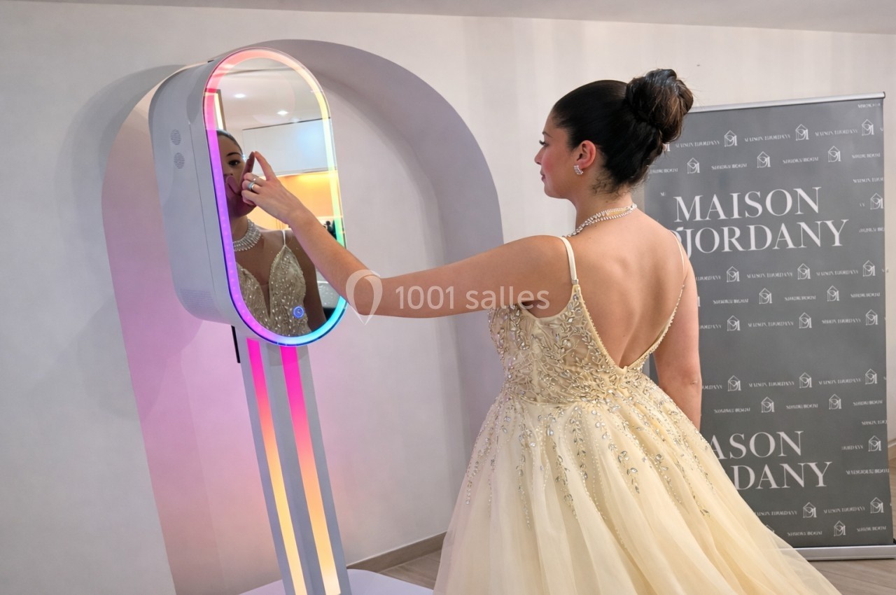 Une femme en robe de soirée beige interagit avec un miroir lumineux dans un espace intérieur élégant.