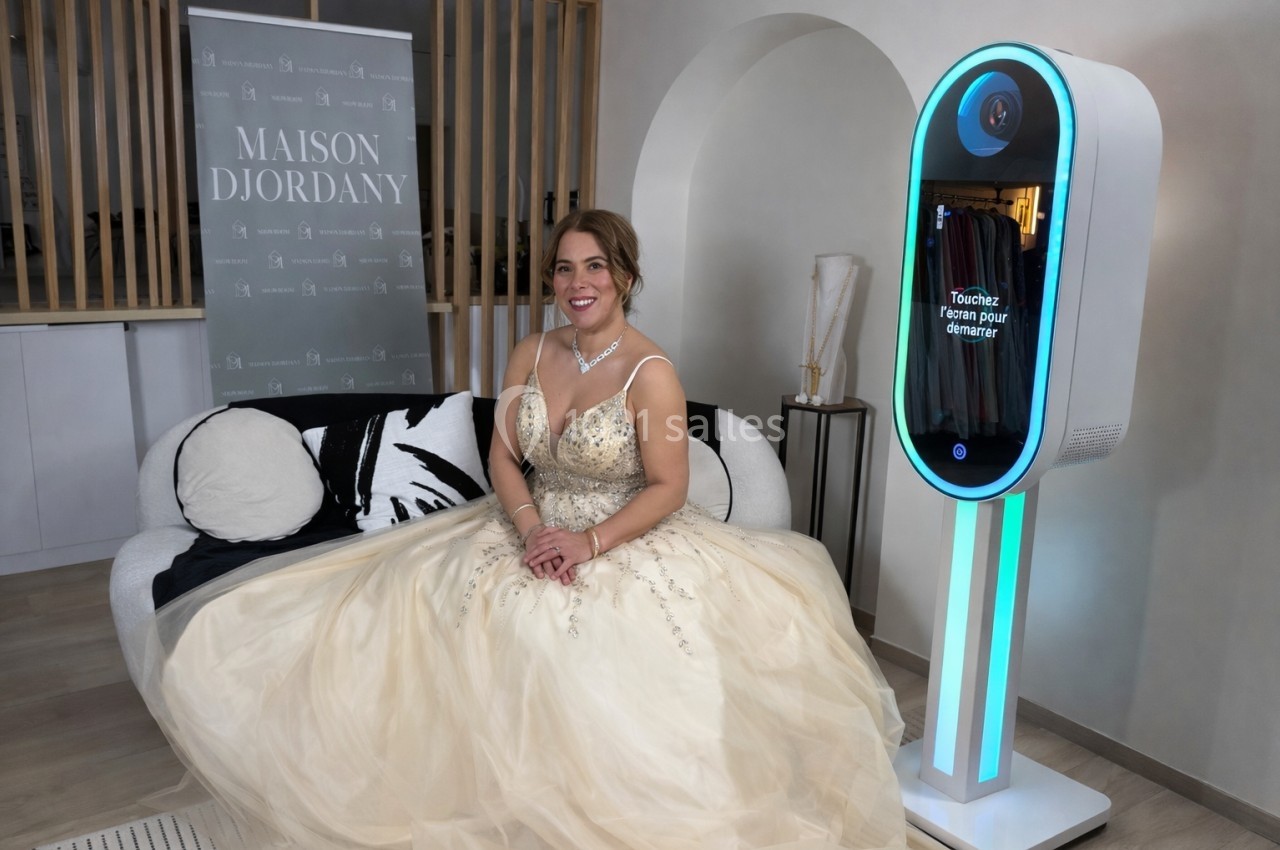 Une femme en robe de soirée beige est assise sur un canapé, près d'une borne interactive lumineuse.