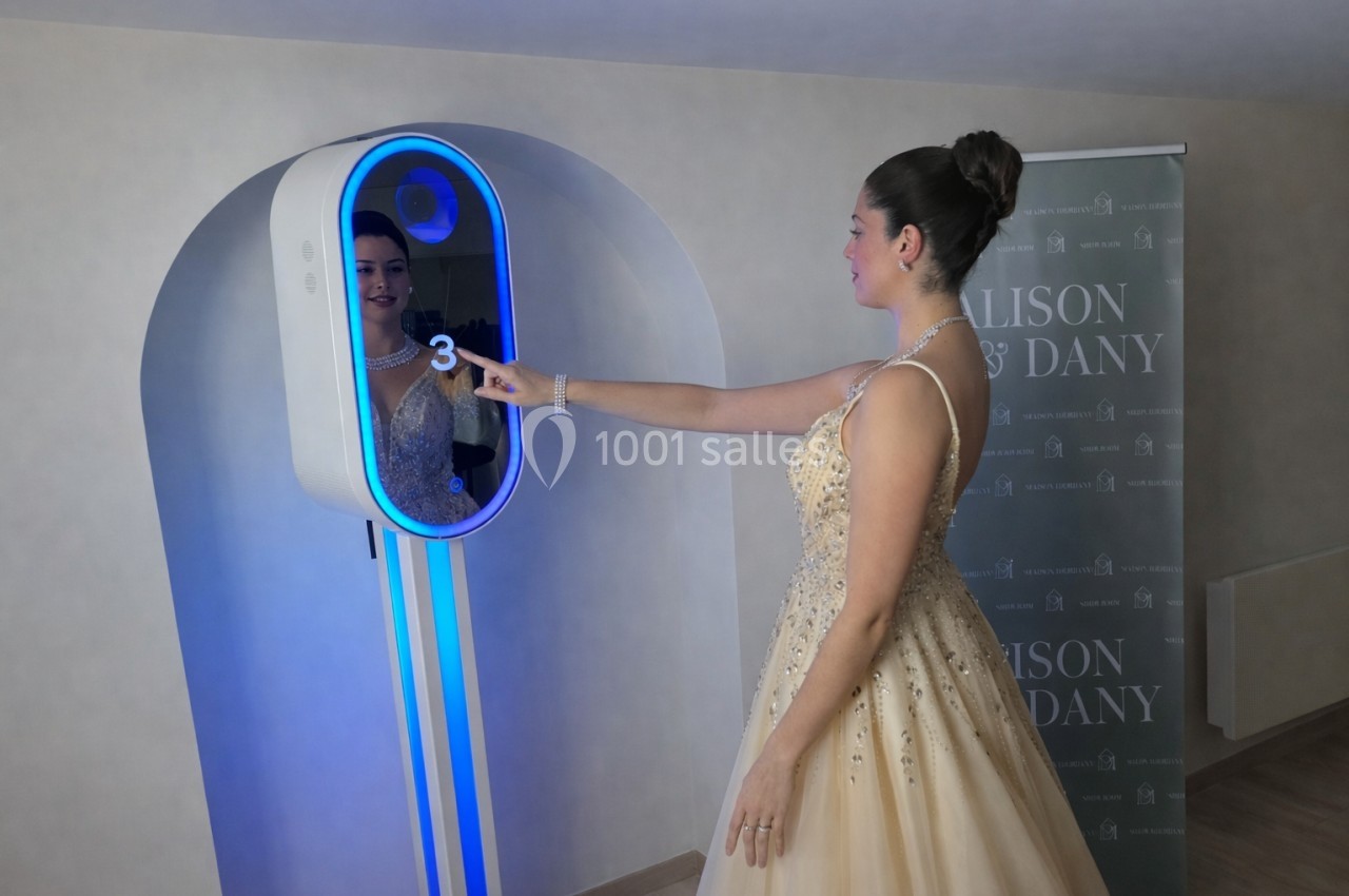 Une femme en robe de soirée interagit avec un photobooth lumineux dans un espace intérieur.