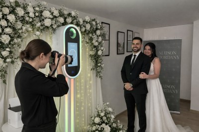 Deux personnes souriantes posant avec des accessoires festifs devant un fond scintillant rose.
