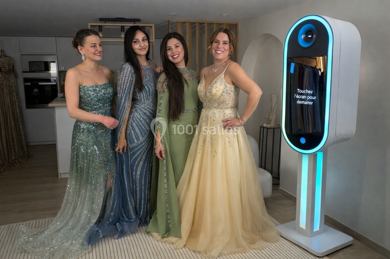 Quatre femmes en robes de soirée posent souriantes à côté d'une borne interactive lumineuse dans un intérieur élégant.