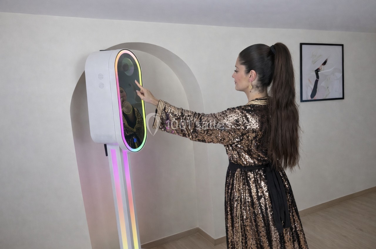 Une femme en robe à paillettes interagit avec un appareil lumineux vertical dans une pièce sobrement décorée.