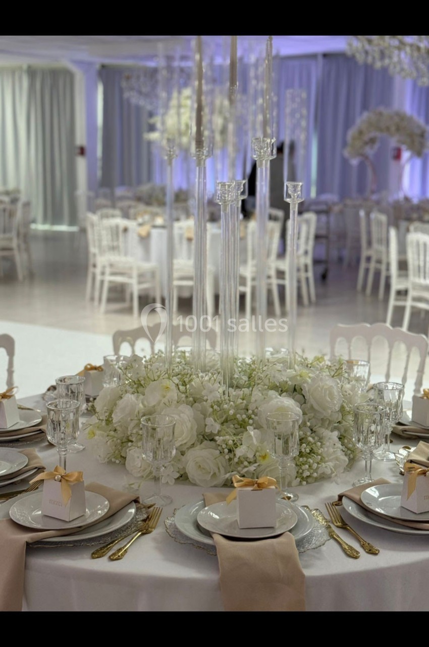 Table élégamment dressée avec des fleurs blanches, bougies hautes et couverts dorés dans une salle de réception.