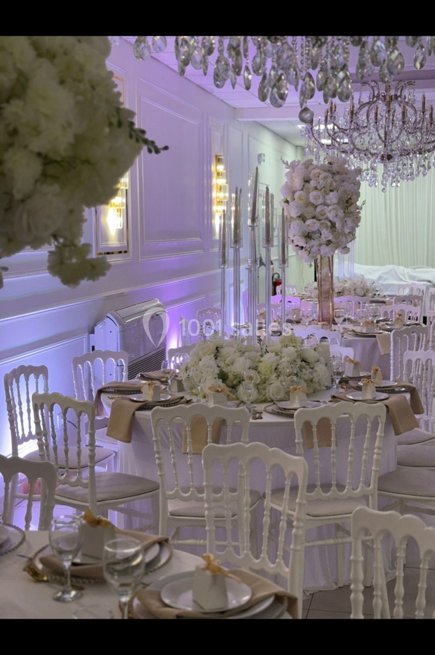 Salle de réception élégante décorée avec des tables rondes, des chaises blanches et des compositions florales blanches.