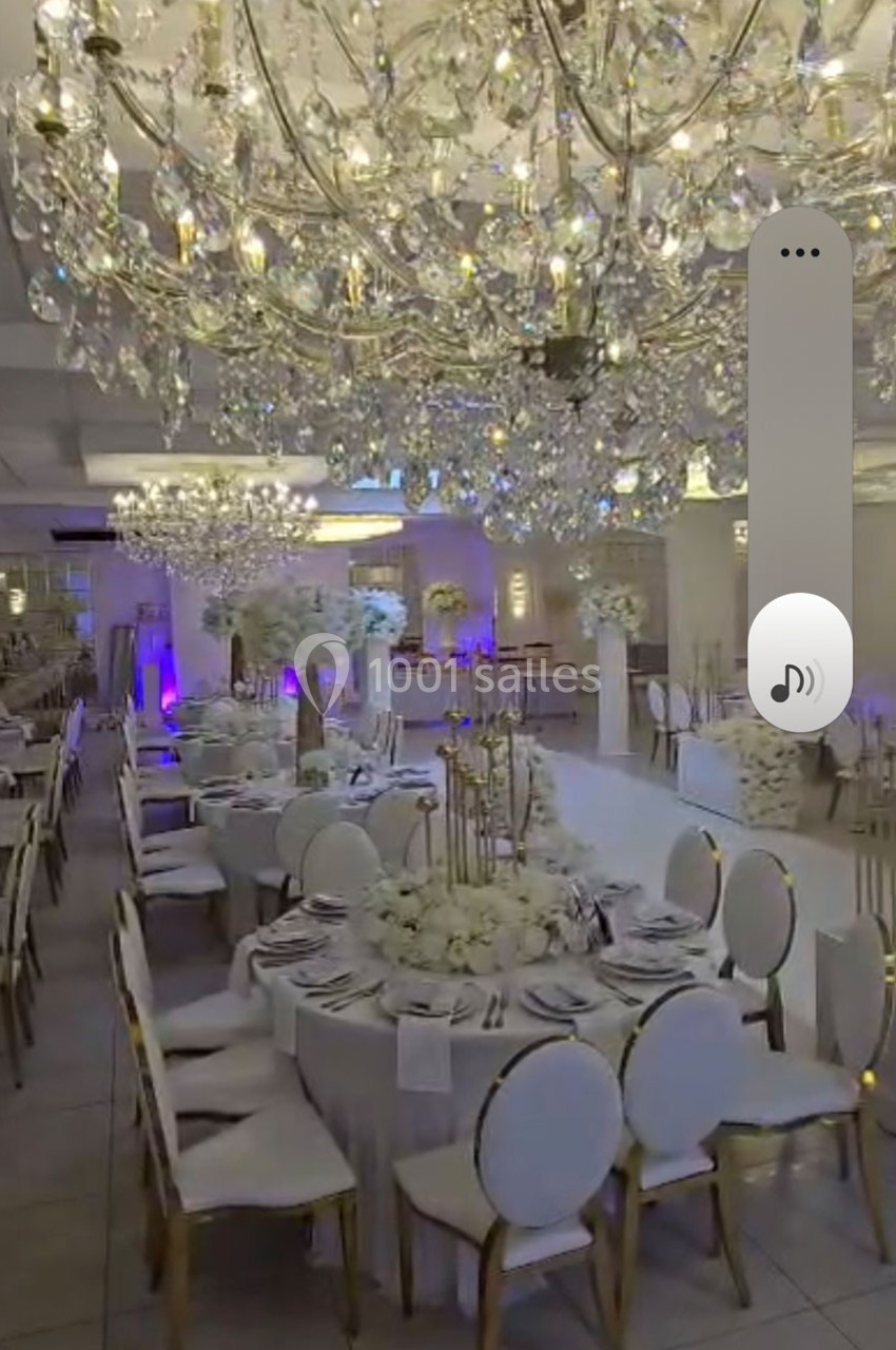 Salle de réception élégante avec tables rondes décorées de fleurs blanches et grands lustres en cristal suspendus.