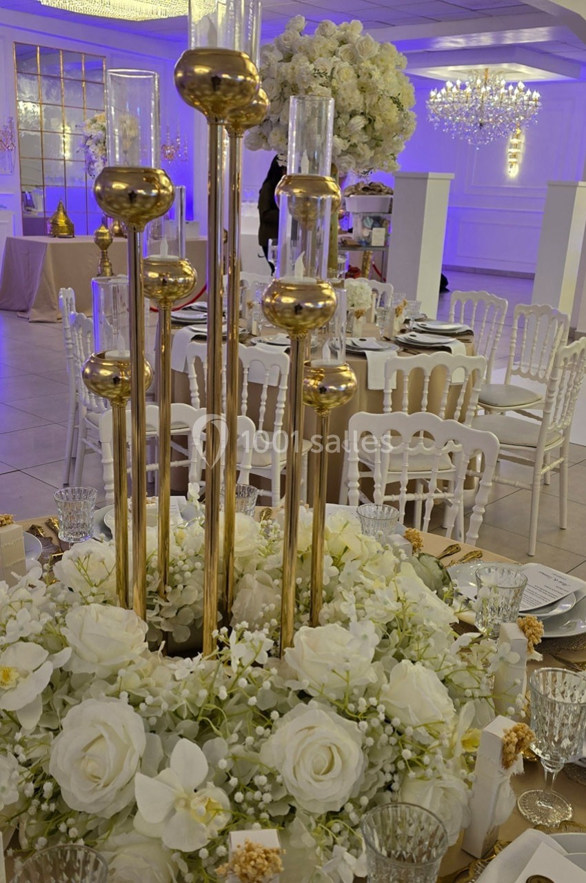 Centre de table élégant avec bougies dorées, fleurs blanches et décoration raffinée dans une salle de réception.