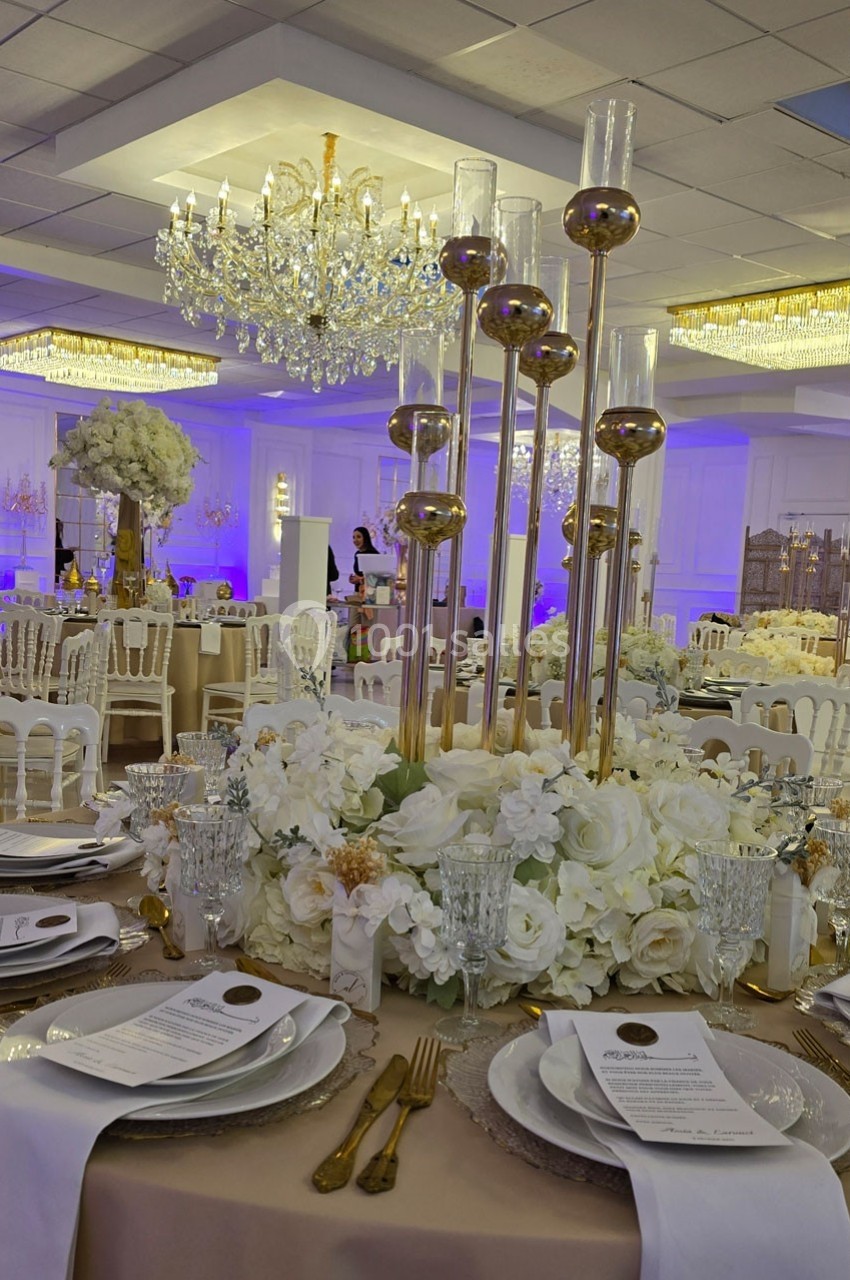 Table élégamment dressée avec des fleurs blanches, chandeliers dorés et vaisselle raffinée dans une salle de réception.