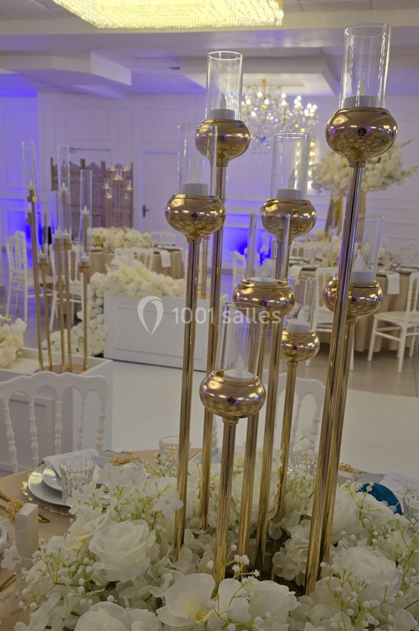 Bougeoirs dorés élancés avec des fleurs blanches en décoration sur une table dans une salle de réception élégante.