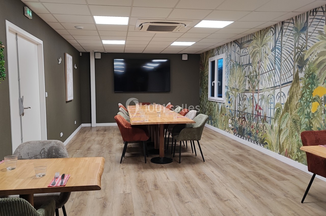 Salle de réunion lumineuse avec une grande table centrale, des chaises colorées et un mur décoré d'une fresque végétale.