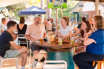 Trois personnes assises sur des canapés en palettes, mangeant des glaces en terrasse par une journée ensoleillée.