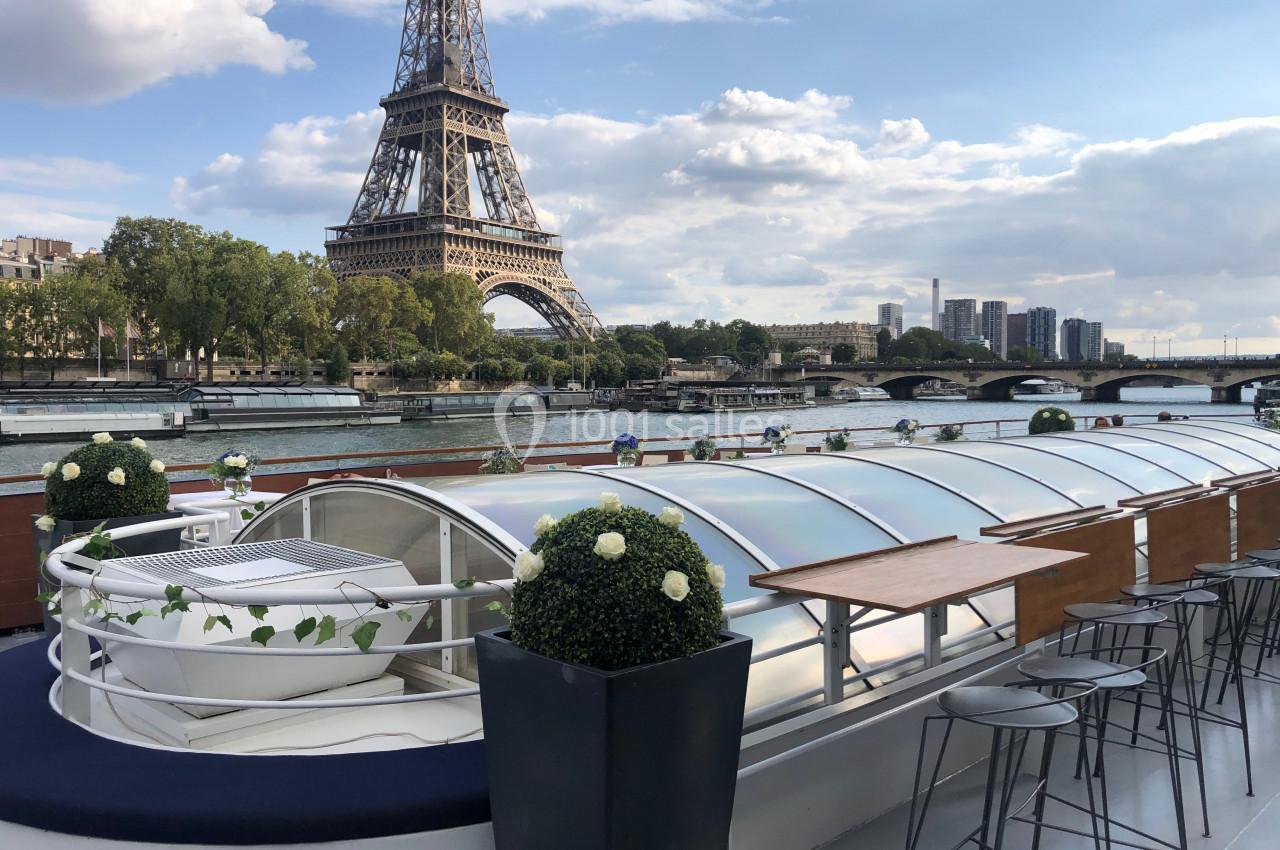 Vue depuis le pont d'un bateau sur la Seine, avec la tour Eiffel en arrière-plan et des tables aménagées.