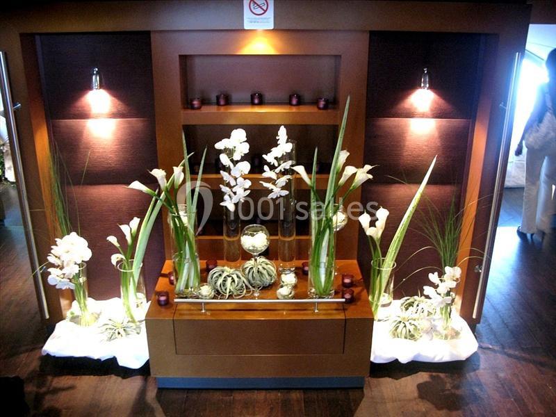 Arrangement floral avec des orchidées blanches et des plantes vertes disposées sur un meuble en bois éclairé.