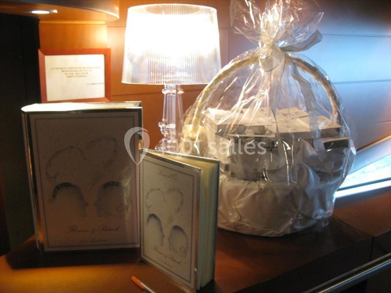 Un panier cadeau emballé, deux livres posés à côté et une lampe allumée sur une table en bois.